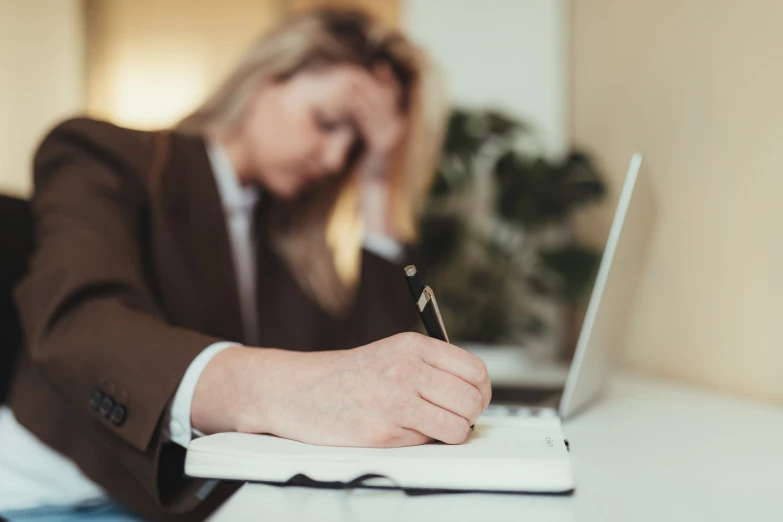 a person at a desk writing in front of a laptop