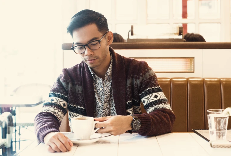 a man is sitting at a table holding a coffee cup