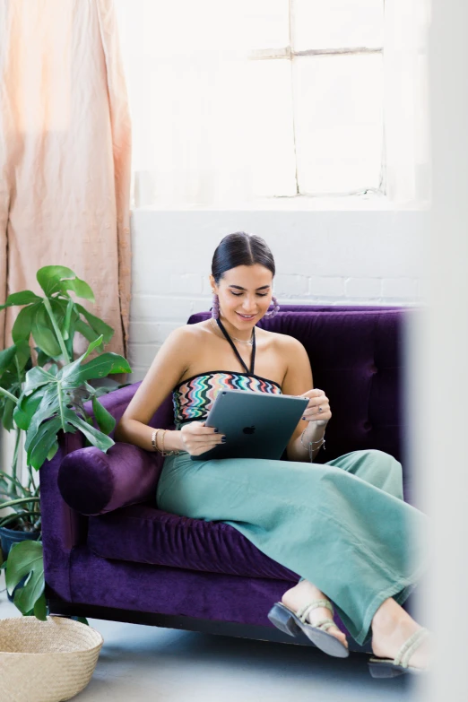 a woman sits in a purple chair using her tablet