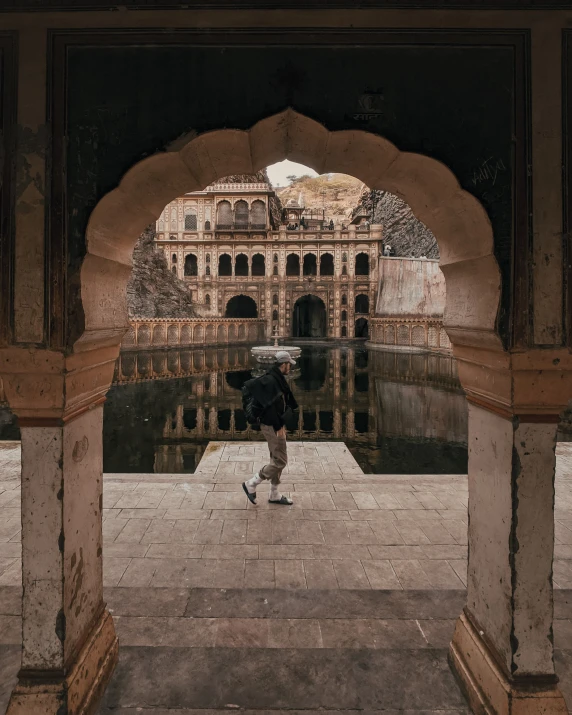 a woman standing in an archway by a building with water and arches