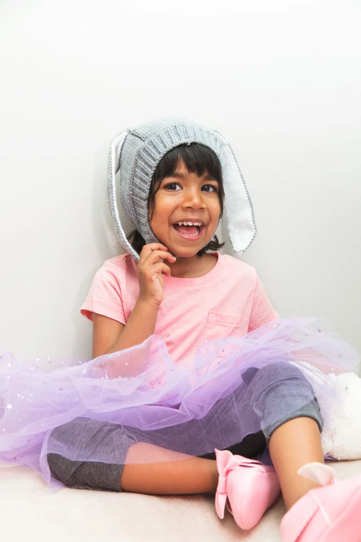 a little girl in pink and a hat sitting on the floor