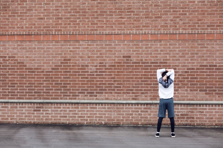 a man standing next to a brick wall with his hands on his head