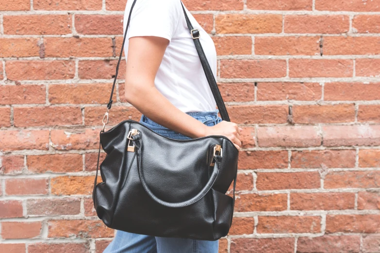 the woman is carrying her black purse next to a brick wall