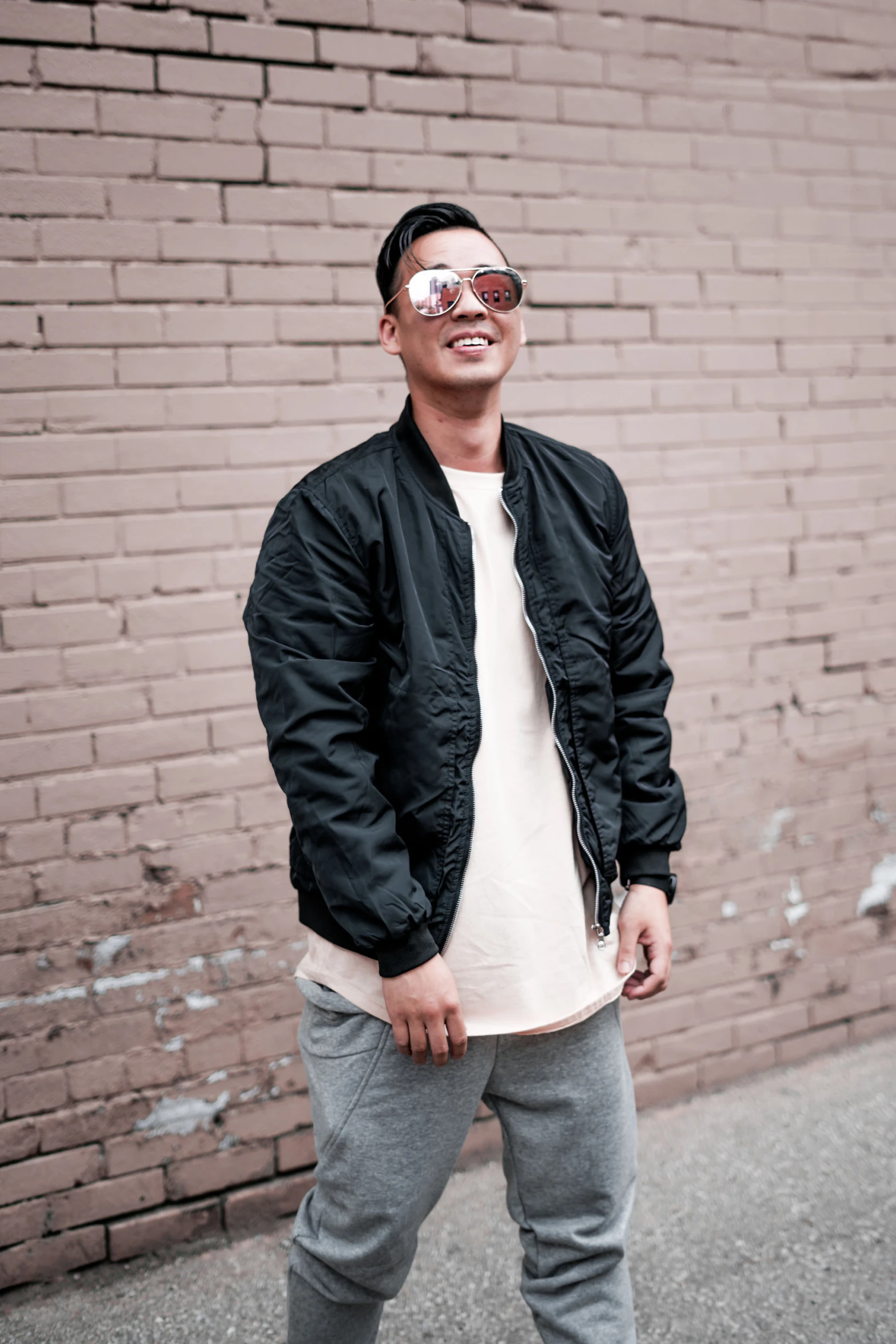 a young man in a black jacket and shades posing in front of a brick wall