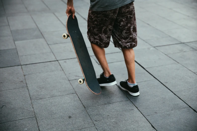 a boy in grey shirt and khakis carrying a skateboard