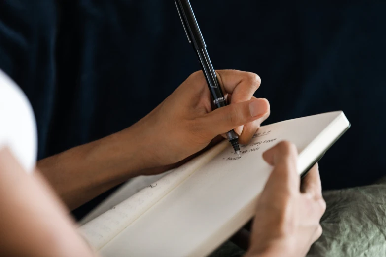 a person holds the pen while holding a notebook