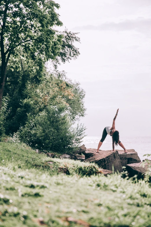 a woman doing yoga on a rock by the water