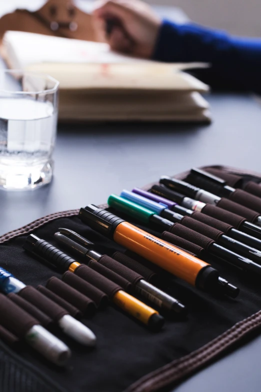 a table filled with pens and notebooks sitting next to a glass