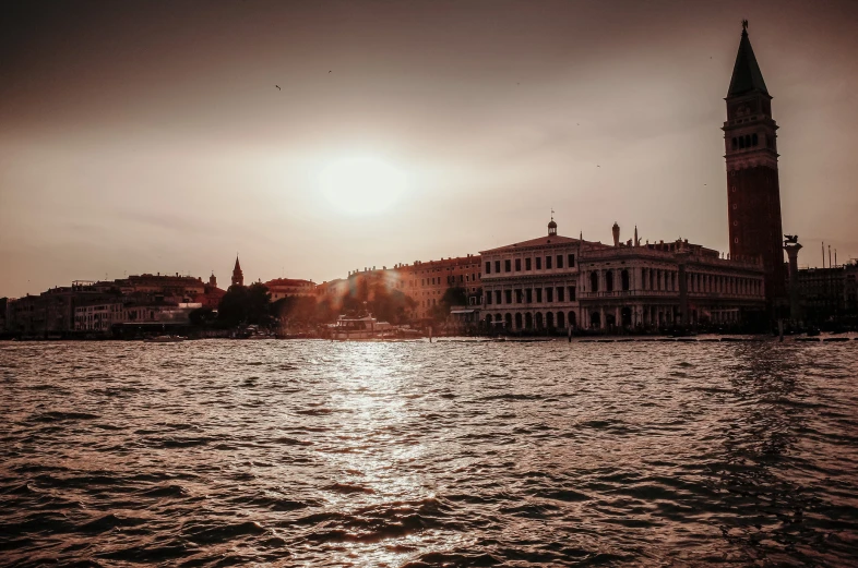 a church and the sun shine brightly over some buildings from the water