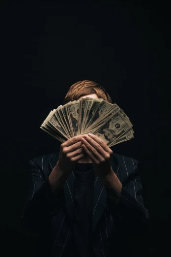 a man covering his face with $ 50 bills