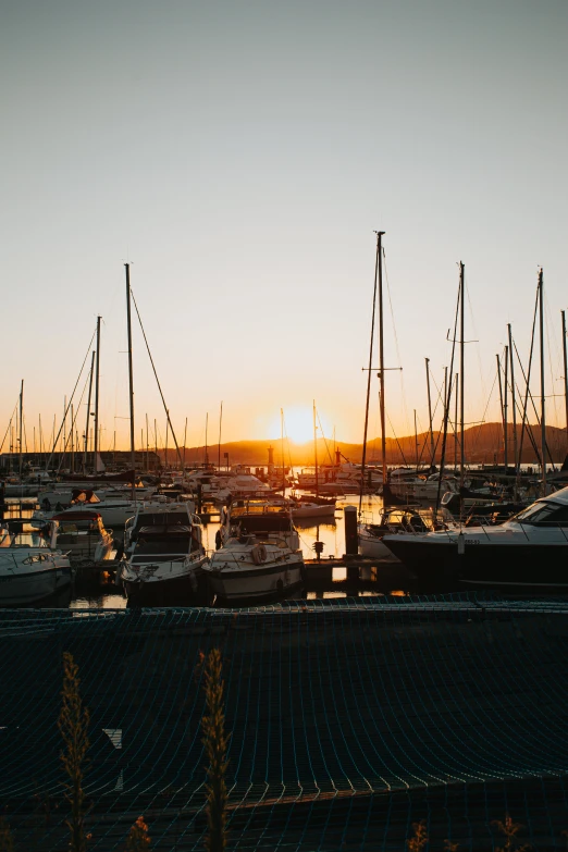 the sun is setting on the yachts docked at the marina