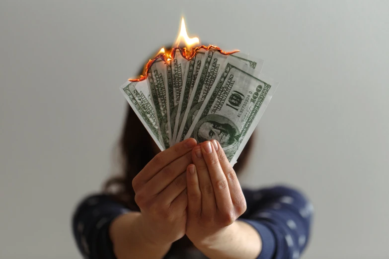 woman in a blue sweater holding up several burning bills