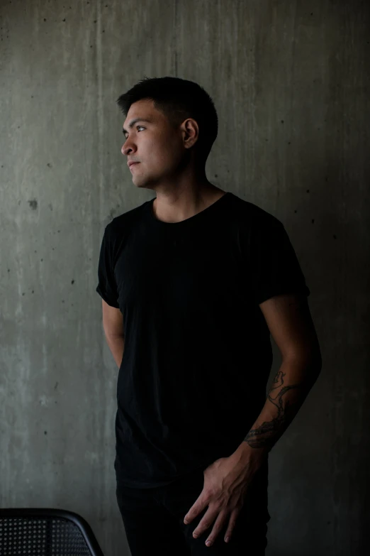 a man with black hair is standing in front of a concrete wall