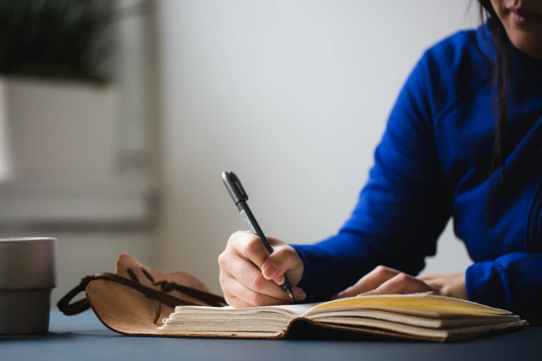 woman writing in an open book with a black pen