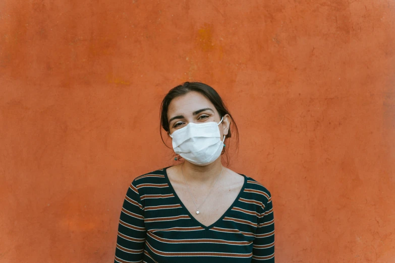 a woman with a white mask on standing in front of a red wall