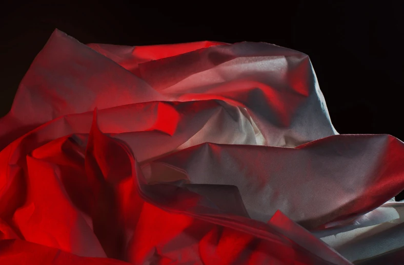 red silk fabric being rolled up in a dark room