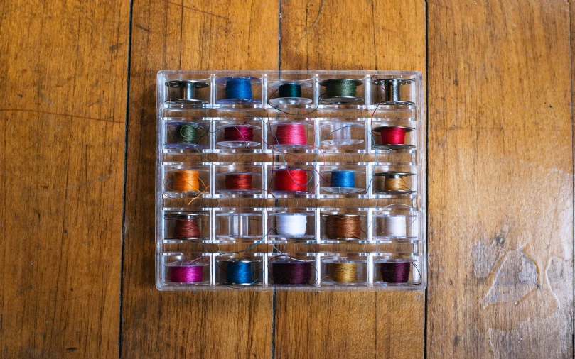 a plastic box is on a wooden floor and holds spools of thread