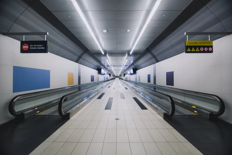 an empty airport with escalators, light and a sign