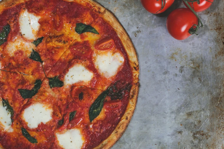 a pizza on a piece of tin with tomatoes in the background