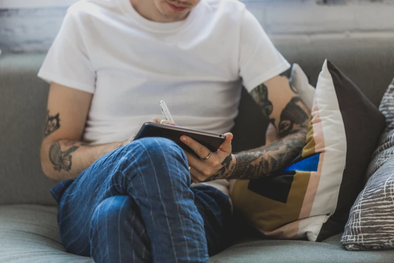 tattooed man with glasses reading a book on a couch