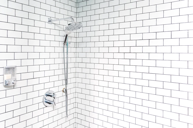 a white tiled shower and the wall is lined with bricks