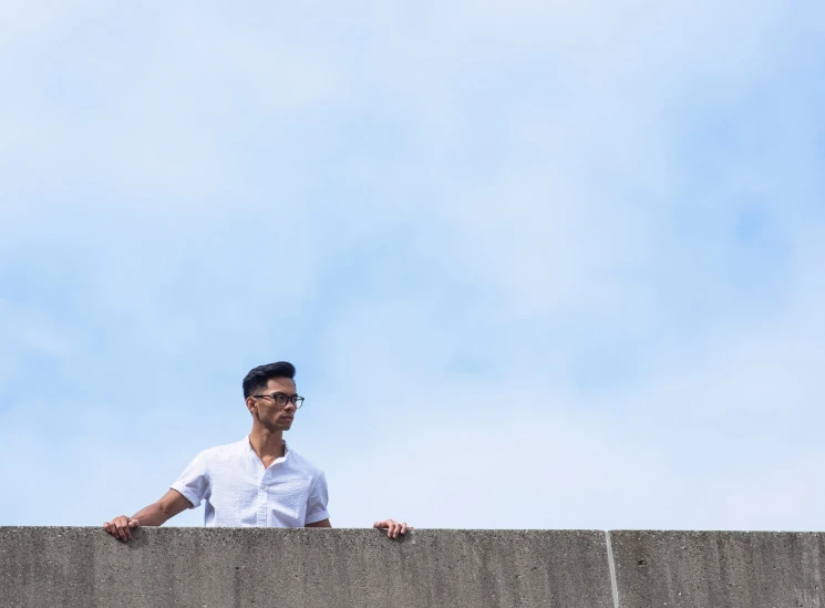 man wearing eyeglasses leaning over edge of cement wall