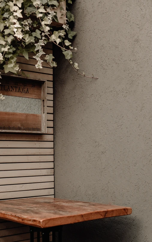 an old wooden table in front of an ivy hanging over the side of the wall