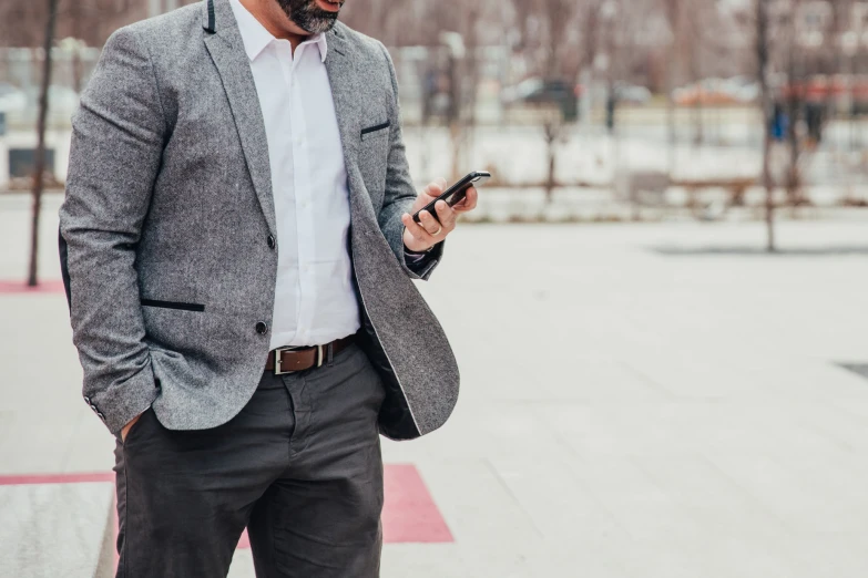 man in suit standing with his hands on his hips looking at his cell phone