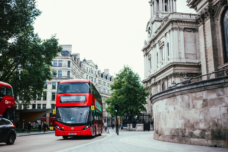 a red double decker bus driving down a street past tall buildings