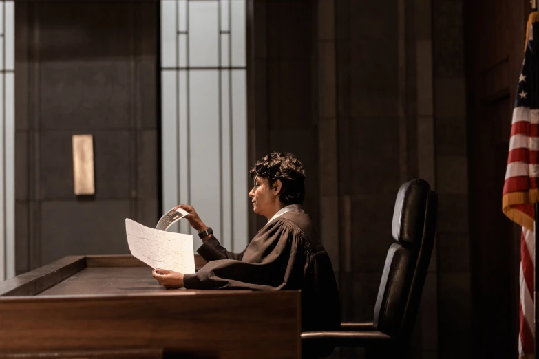 a woman in black robes sitting at a table with papers