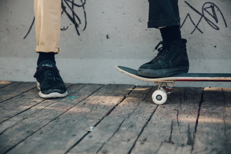 the feet are standing on the skateboard against the wall