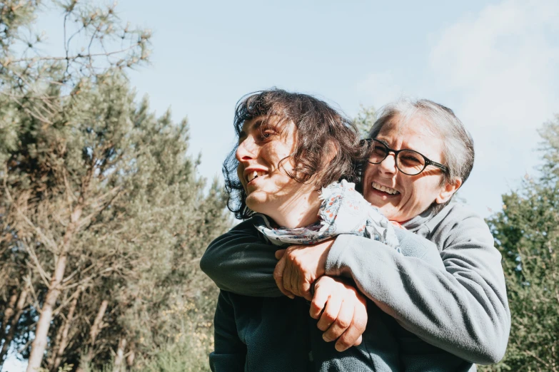 an elderly woman hugging another older woman with trees in the background