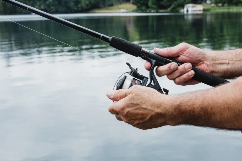 man in gray shirt and white cap holding up a black fishing pole