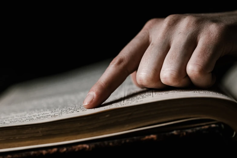 a hand touching an open book on a dark background