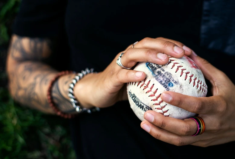 a tattooed arm holding an old baseball in his hands