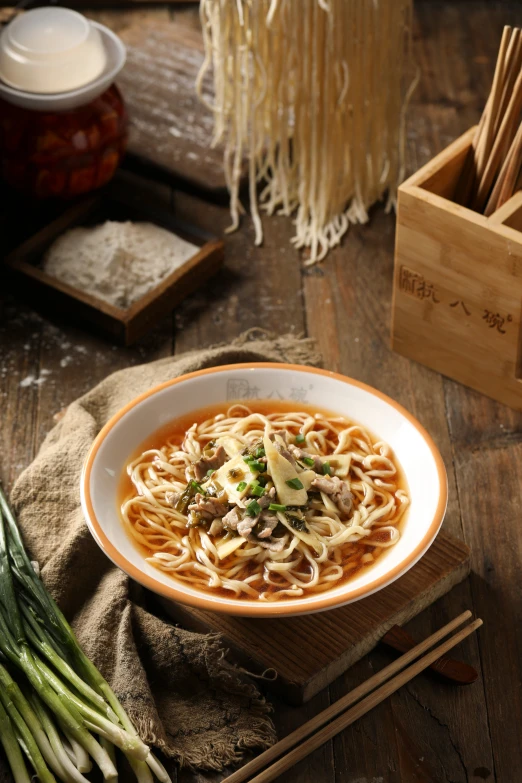 a bowl of soup with noodles and onions and chopsticks on the side