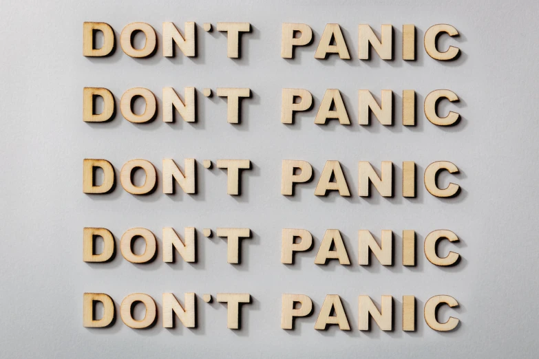 the text don't panic don't panic don't panic and a piece of wood with two letters arranged in front of it