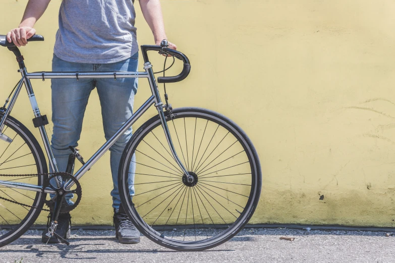 man standing with bicycle against yellow wall with no wheel