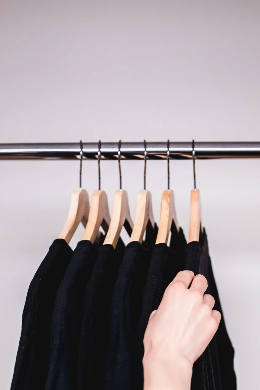 a person is pointing at four shirts on a rack