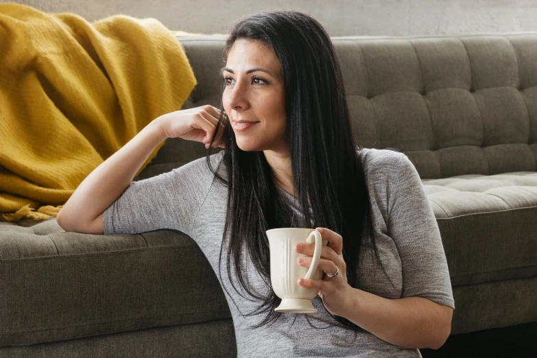 a woman is sitting on the couch drinking her coffee