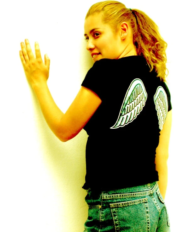 a beautiful blonde woman leaning against a wall wearing a black shirt with angel wings