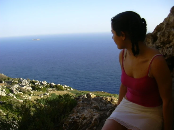 a woman sitting on top of a rock near the ocean