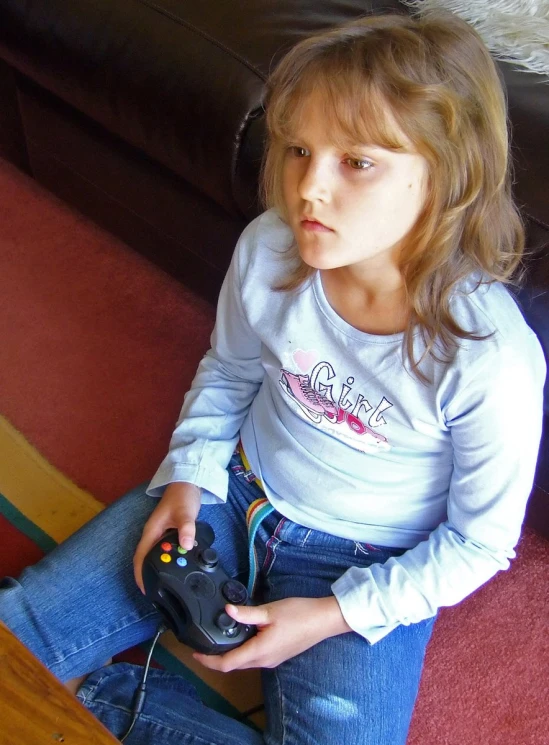 a little girl sitting on a couch holding an electronic device