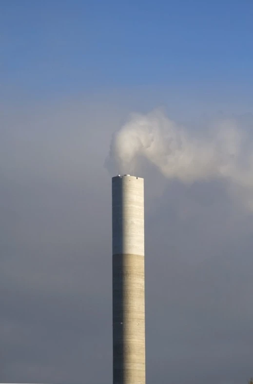 a tall cement building blowing steam in front of a cloud filled sky