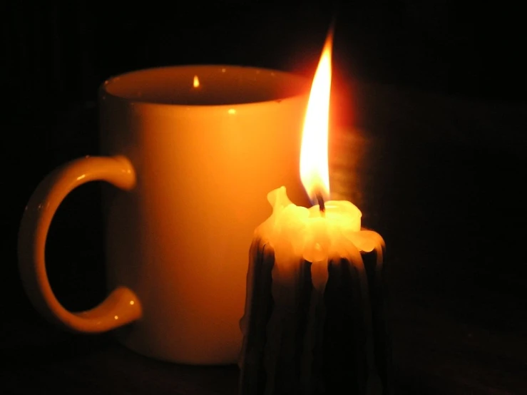 a candle burns brightly next to a cup of tea