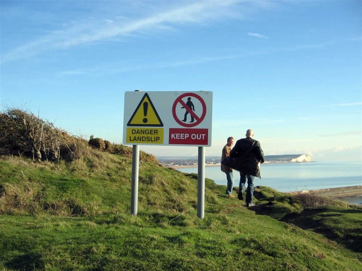 two people walking up a grassy hill to a no walkers keep out sign