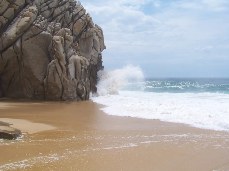 a large rock sticking out of the ocean next to a sandy beach