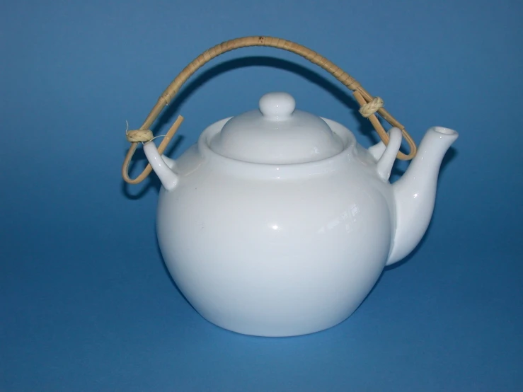 a white teapot with handle and straw handles on a blue surface