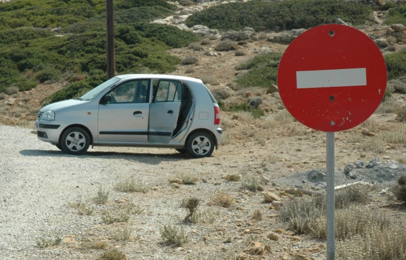 a small compact car is parked by a sign on the side of a dirt road