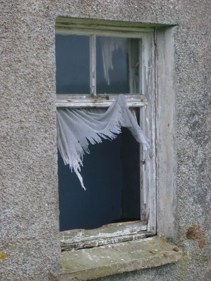 an old window in the wall, with white net hanging from it